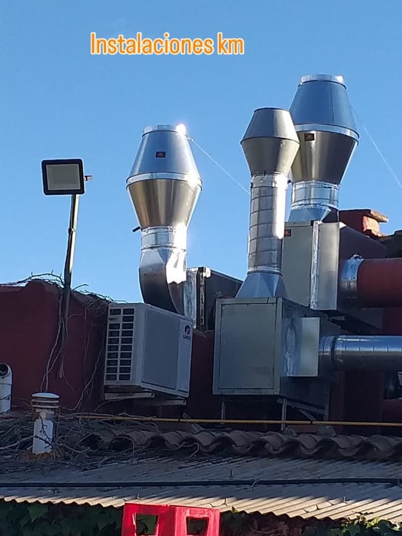 Azotea con conductos de ventilación metálicos, unidad de aire acondicionado y proyector contra un cielo azul.