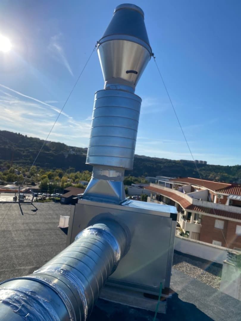 Rejilla de ventilación metálica sobre un tejado, con cables tensores, contra un cielo azul.