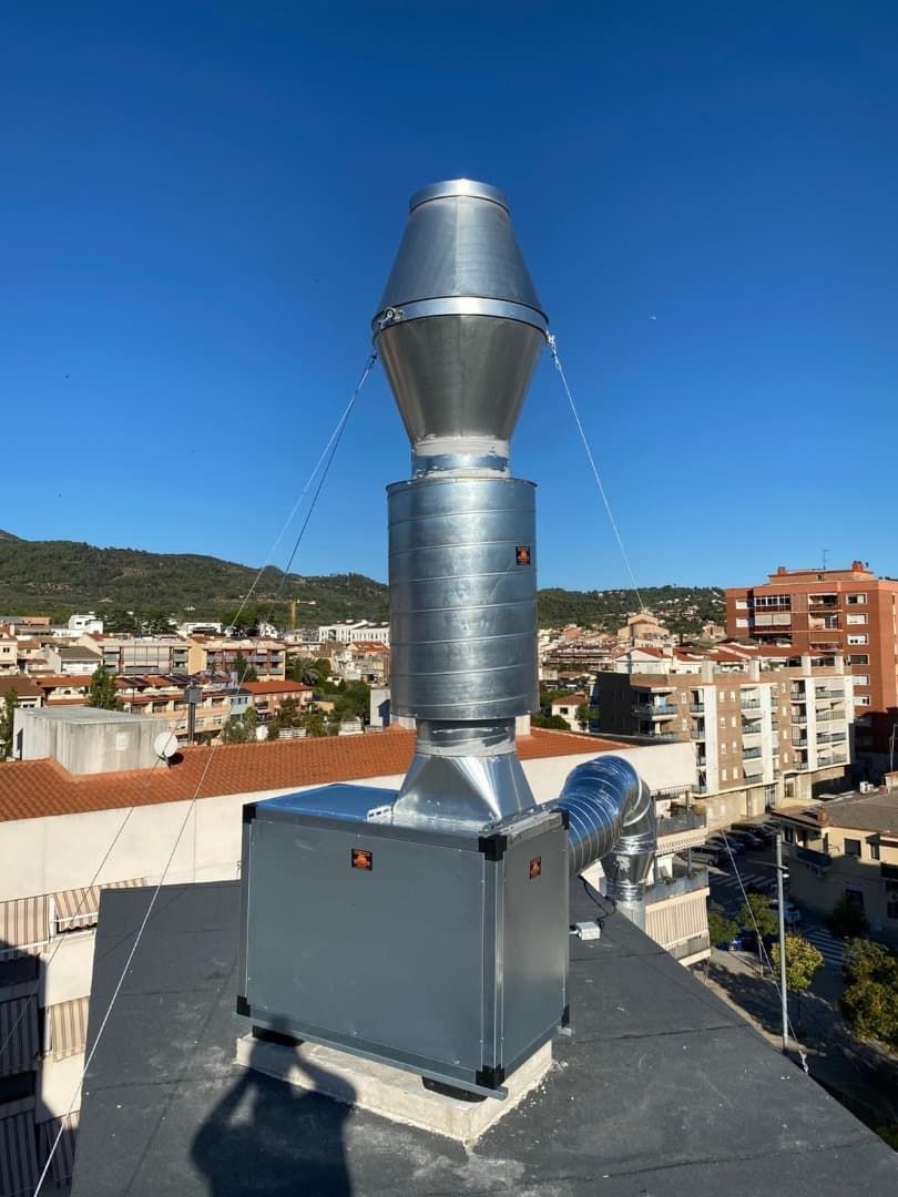 Unidad de ventilación industrial de metal en una azotea con un cielo azul claro y una ciudad de fondo.