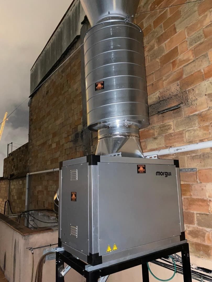 Sistema de filtración de aire de plata en el techo de un edificio de ladrillo, con chimenea de extracción y componentes eléctricos.