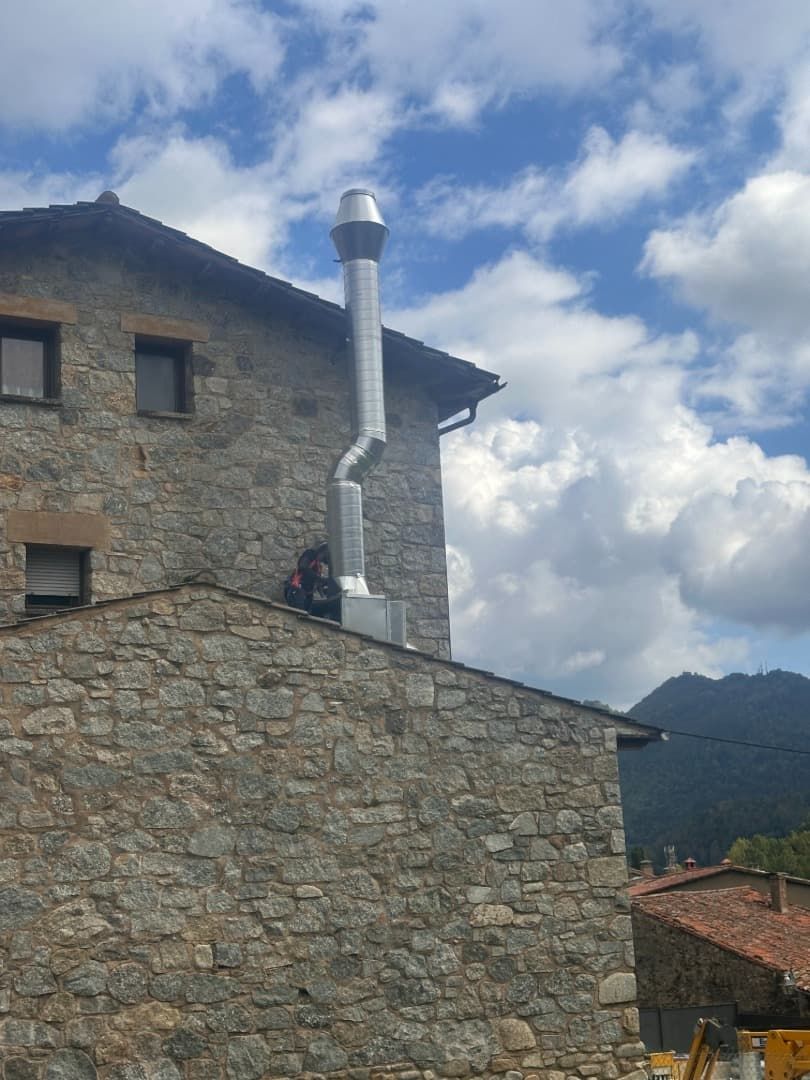 Edificio de piedra con chimenea de metal contra un cielo azul con nubes.