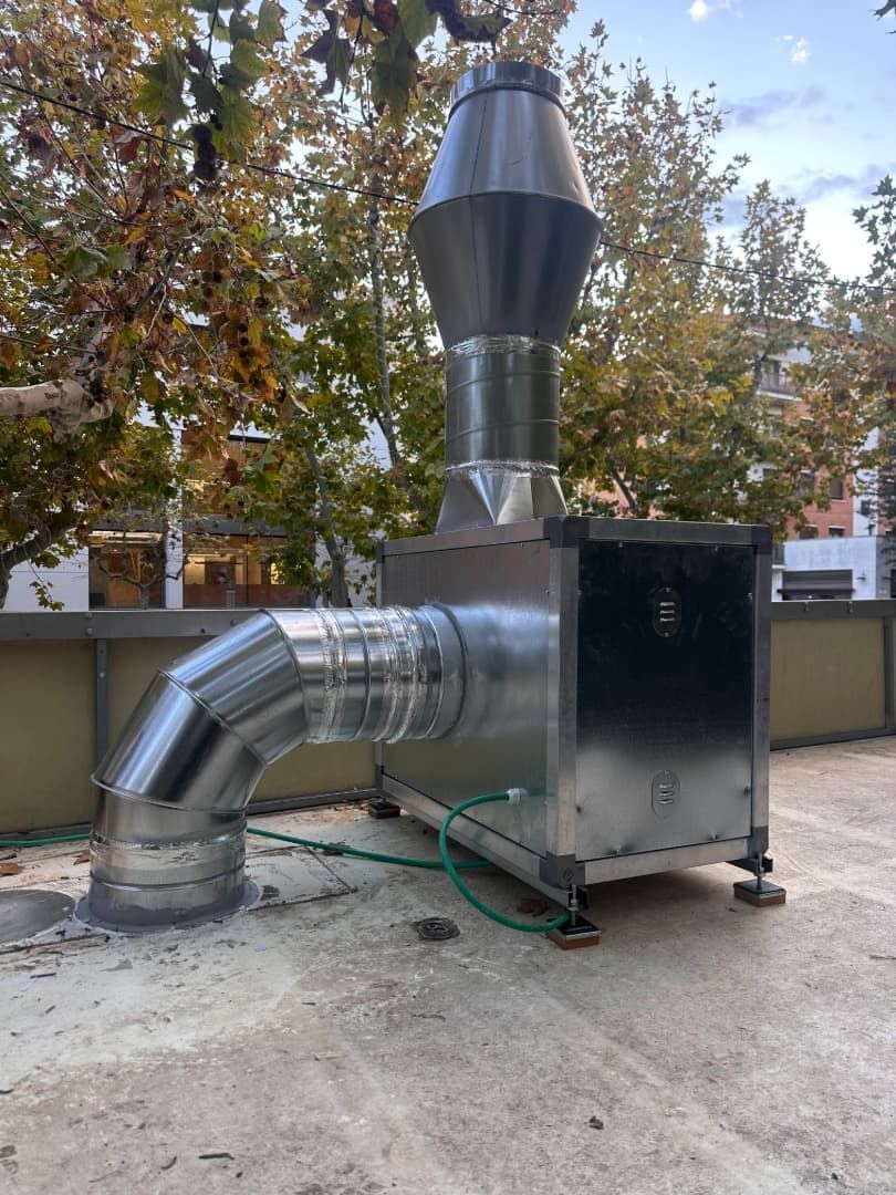 Un sistema de escape de metal con un tubo curvo y una parte superior cónica, en un tejado.