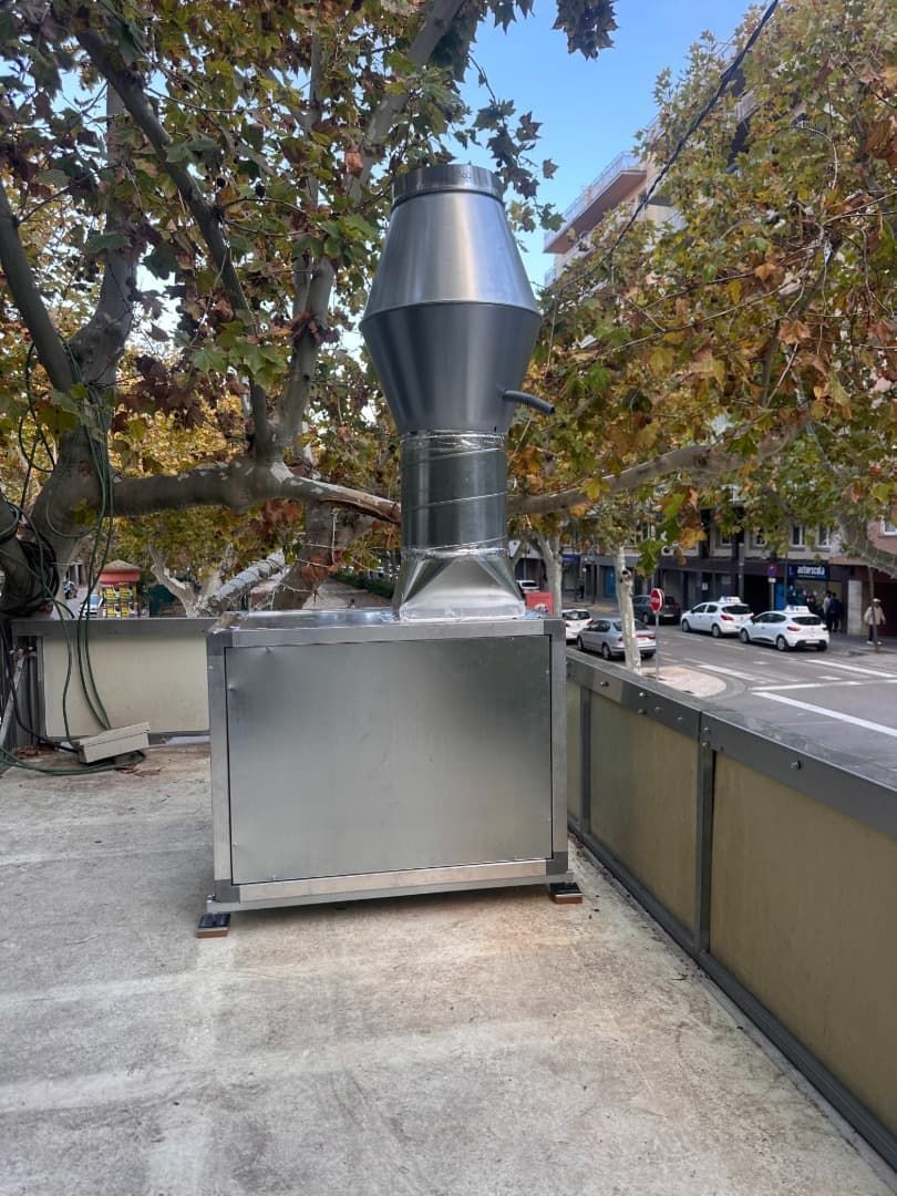 Unidad de ventilación de acero inoxidable en una acera de la ciudad, cerca de una calle arbolada.