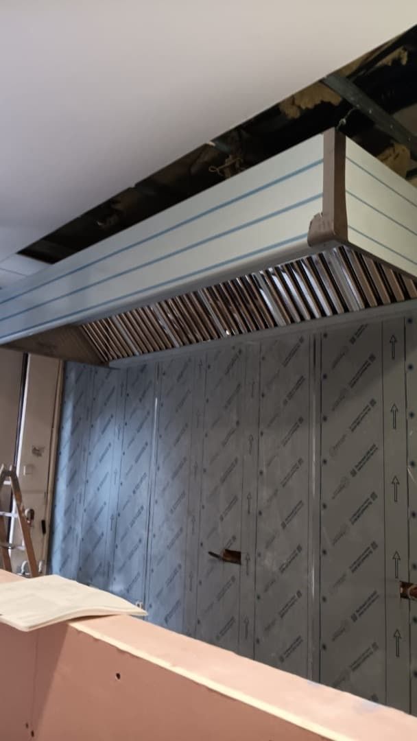 Campana de cocina comercial de acero inoxidable instalada contra pared de acero inoxidable.