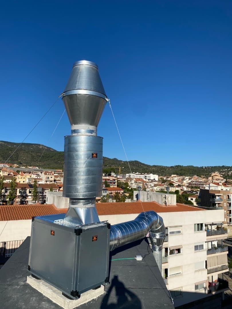 Un sistema de ventilación de metal en una azotea, con una ciudad y un cielo azul al fondo.