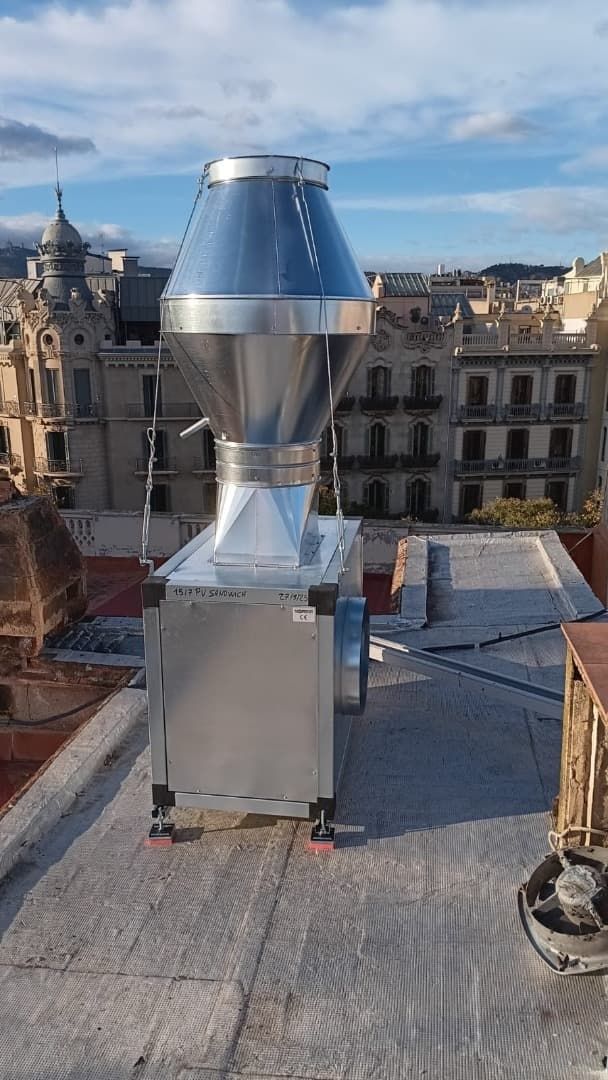 Unidad de extractor industrial metálica en una azotea, con un paisaje urbano y un cielo azul de fondo.