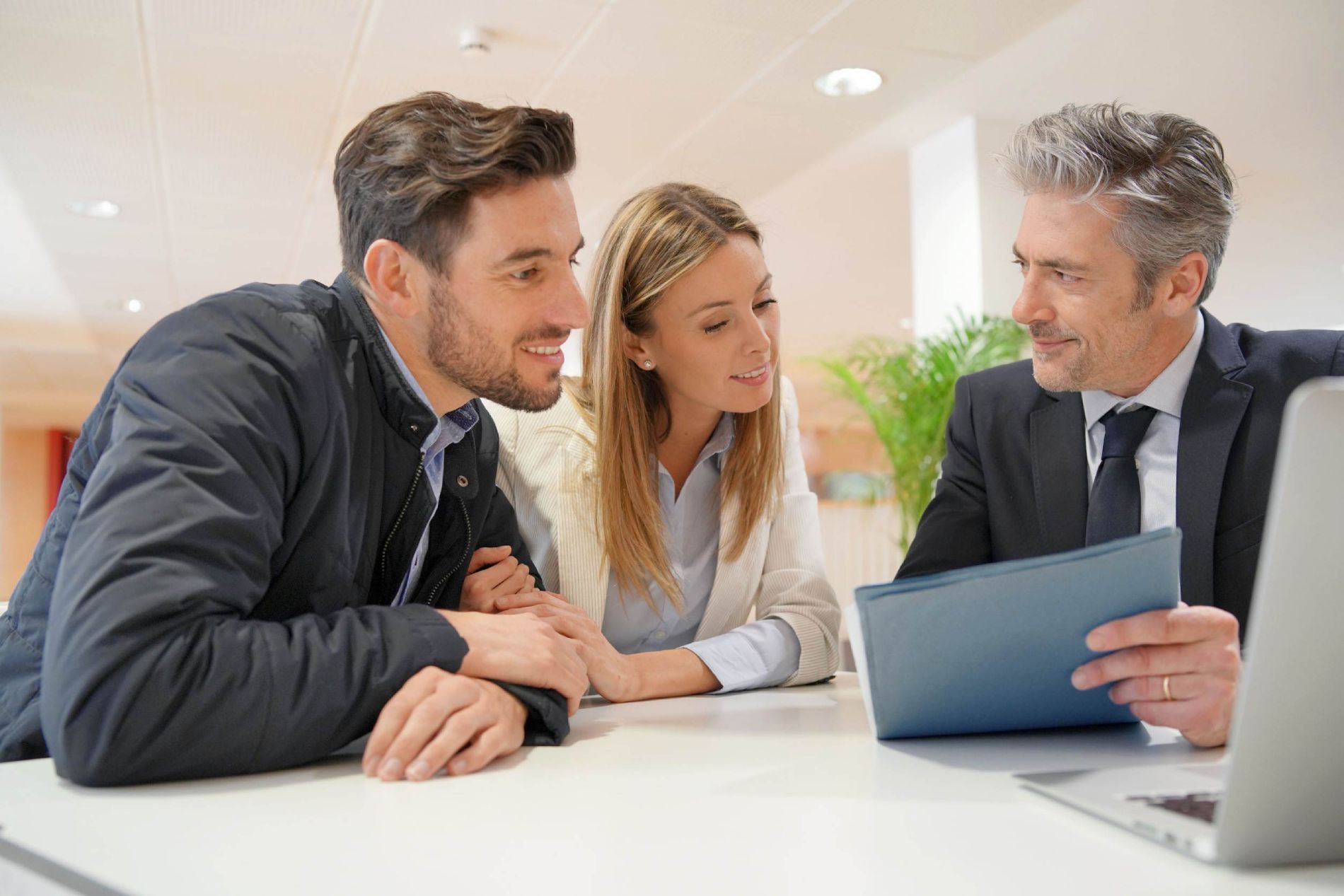 Tres profesionales conversando sobre una tableta en una mesa de oficina bien iluminada.