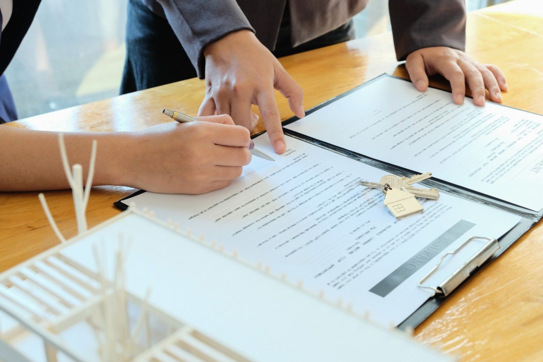 Manos rellenando un formulario en un portapapeles sobre una mesa de madera con papeles y llaves.