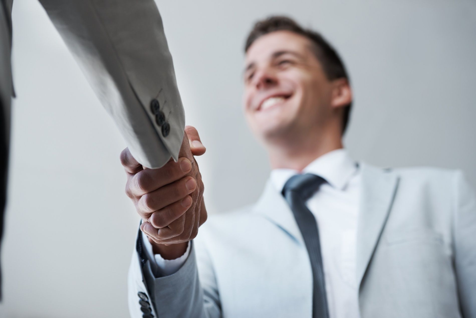 Empresario con traje blanco estrechando manos en una oficina luminosa, sonriendo hacia arriba.