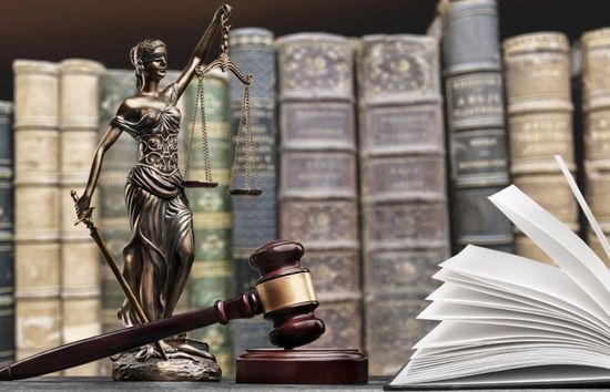Estatua de la justicia con mazo y libro abierto frente a libros de leyes.