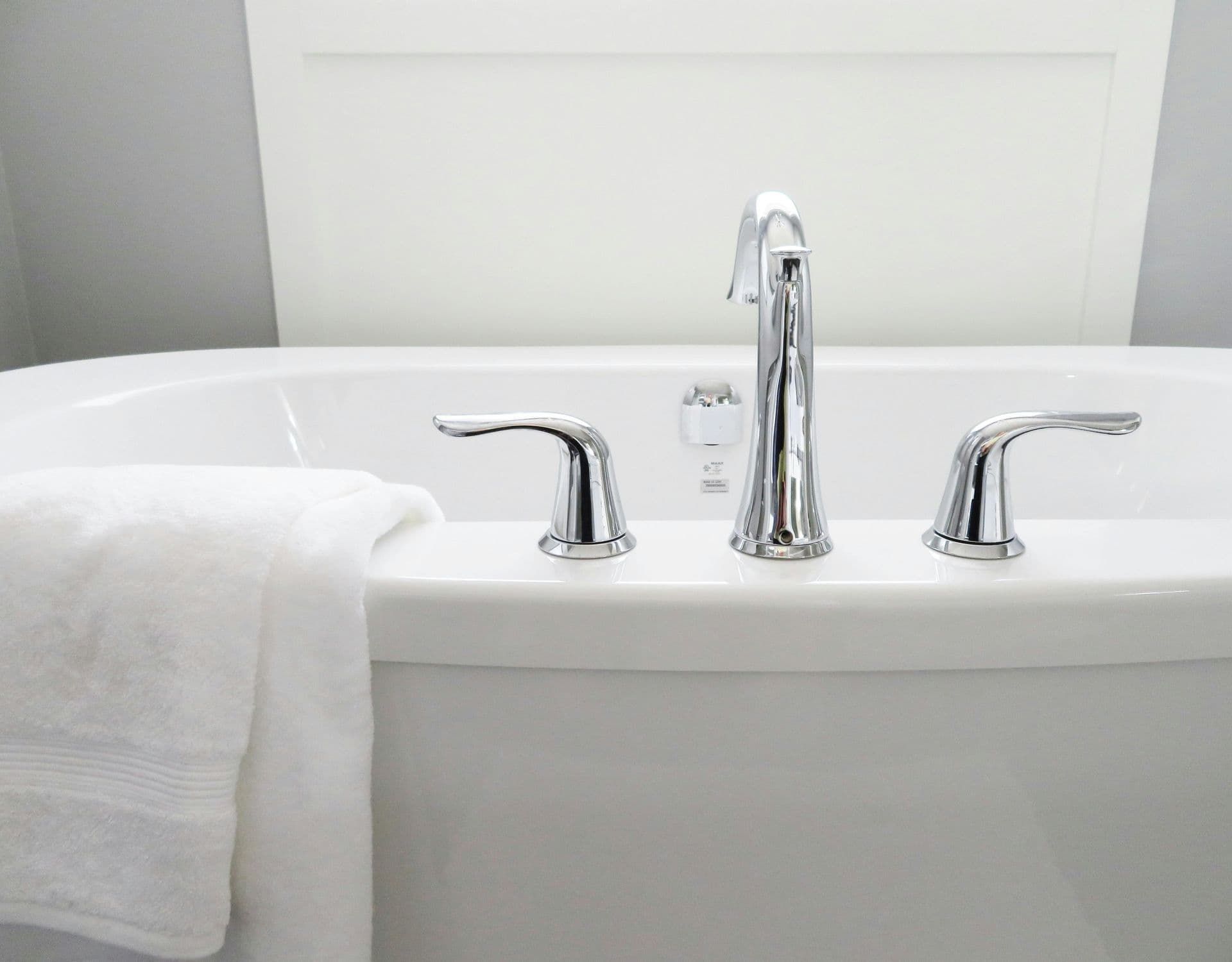 Bañera blanca con grifo y manijas cromadas, una toalla blanca doblada.