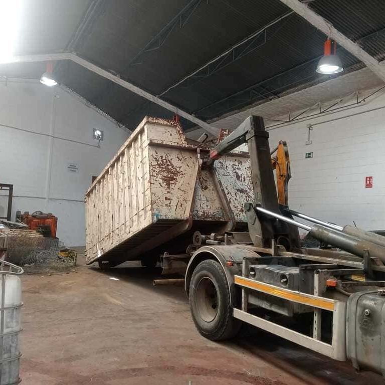 Se está cargando un contenedor de basura en un camión en un almacén.