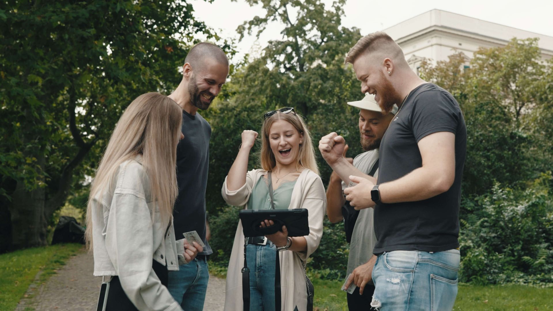 Eine Gruppe von Leuten steht in einem Park und schaut auf ein Tablet.