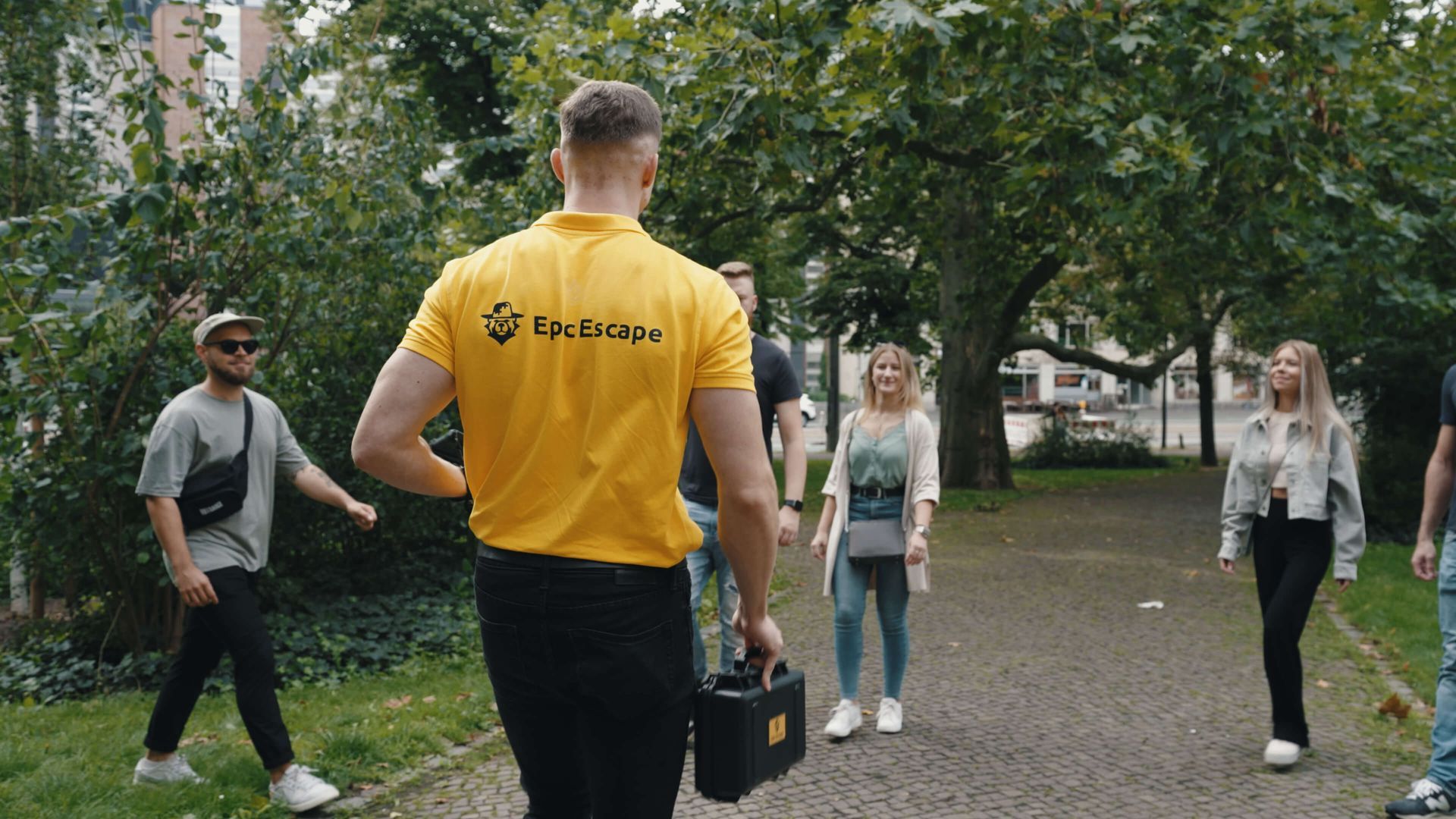 Ein Mann in einem gelben Hemd geht mit einer Gruppe von Menschen einen Weg entlang.
