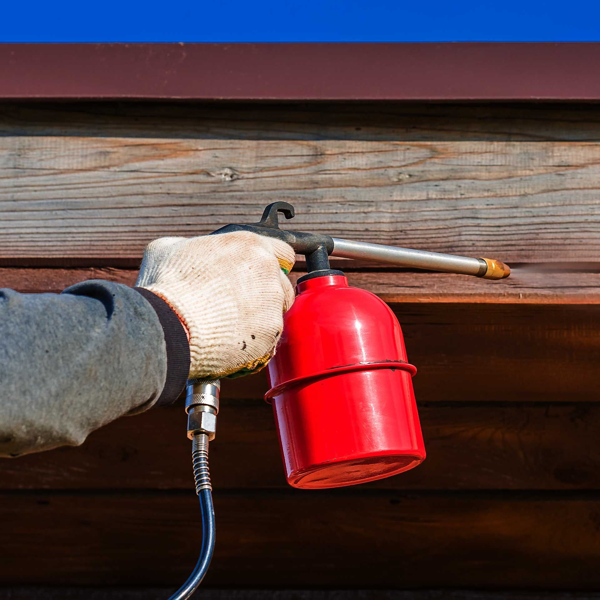 Les mains d'un charpentier appliquant un traitement sur le bois à l'aide d'un aspergeur
