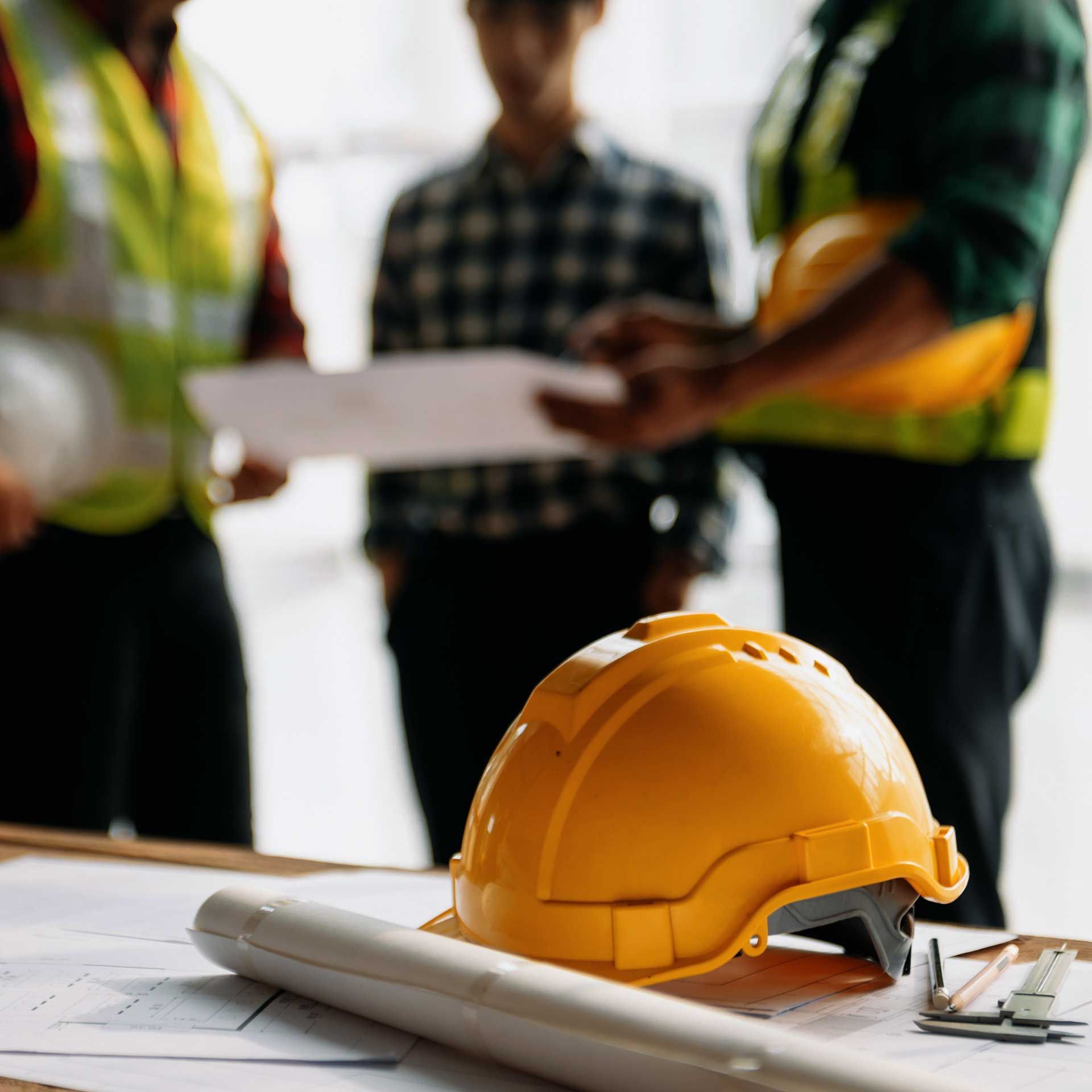 Un casque et des plans d'architecte sur fond de réunion d'ouvriers