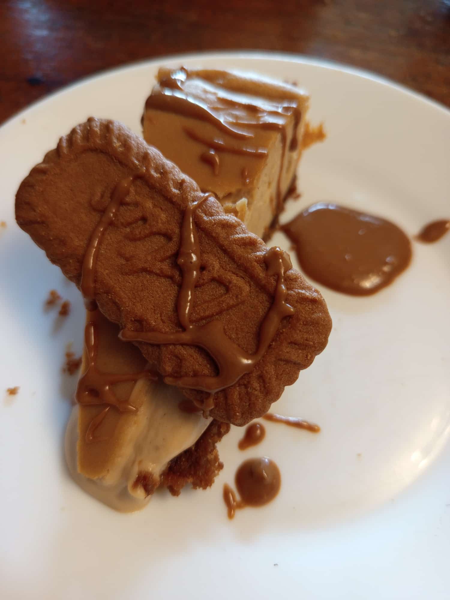 Un plato blanco cubierto con un trozo de pastel y una galleta de loto.