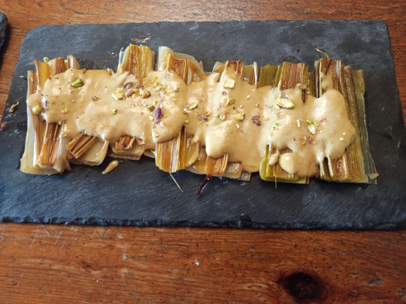 Un plato de comida con salsa y pistachos sobre una mesa de madera.