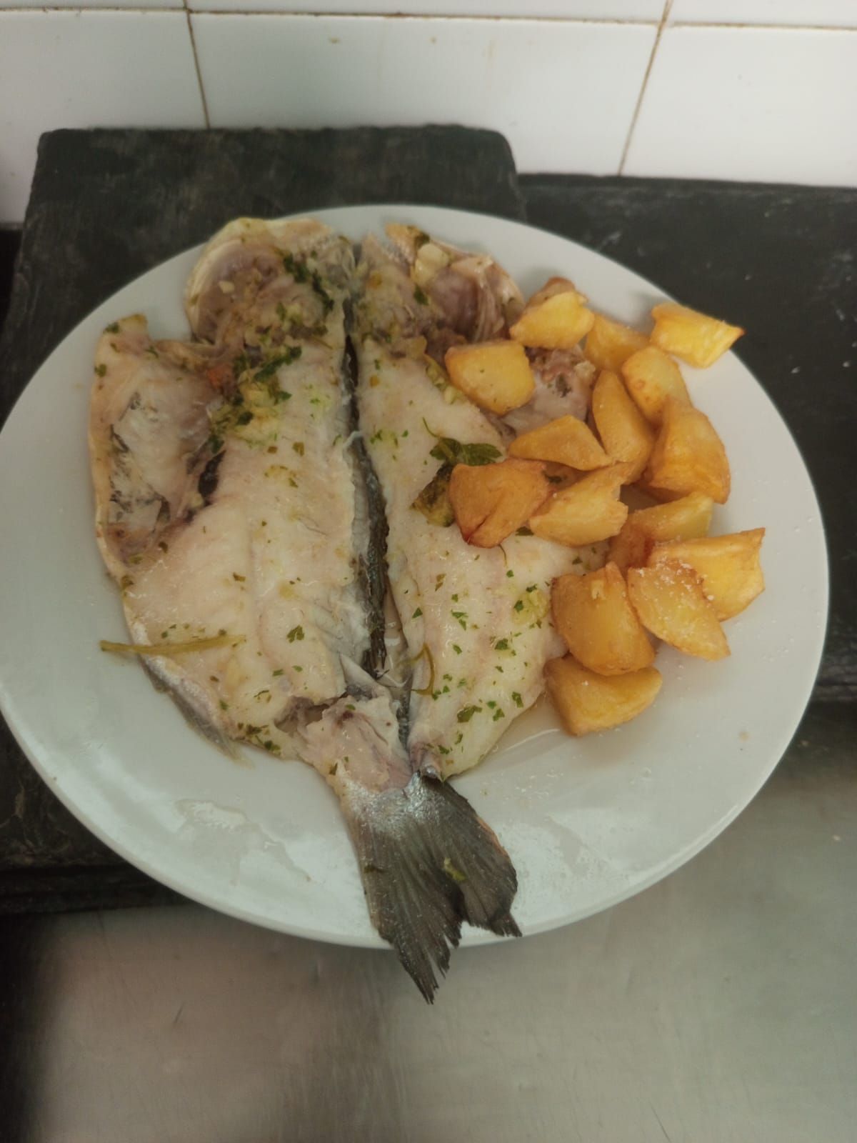 Un plato blanco cubierto con pescado y patatas sobre un mostrador.