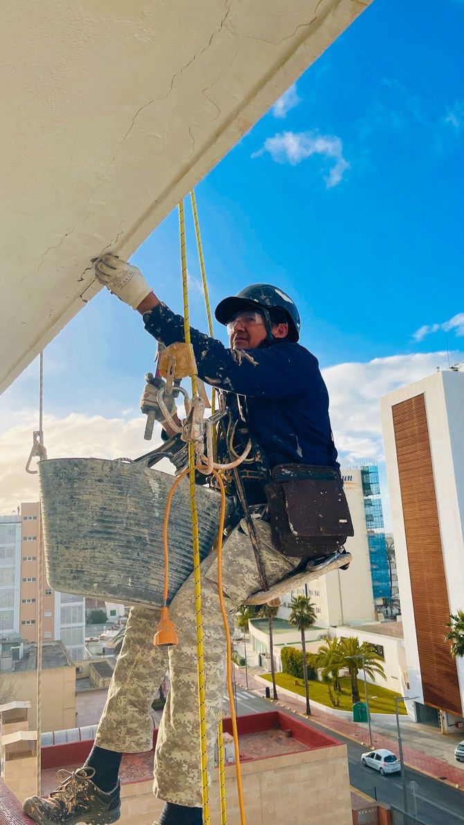 Un hombre está colgado de una cuerda y pintando un edificio.