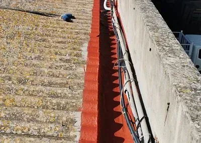 Se está pintando de rojo una canaleta en el lateral de un edificio.