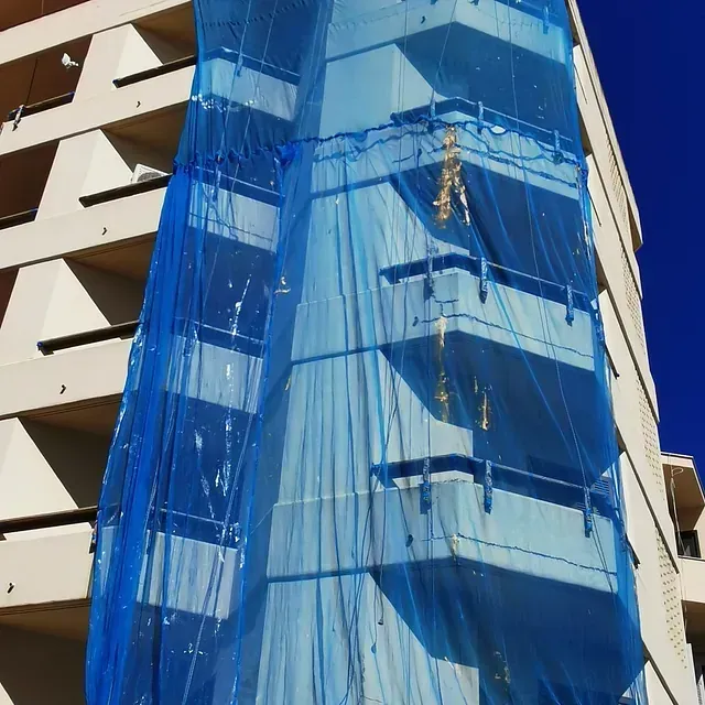 Una lona azul cubre un edificio con balcones.