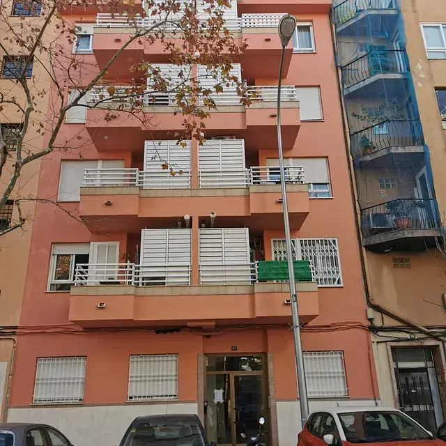 Un edificio con un coche rojo aparcado delante.