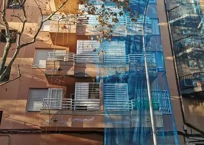 Un edificio con muchas ventanas y balcones está cubierto de andamios azules.