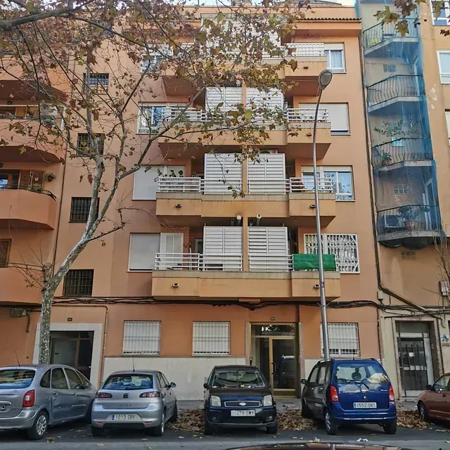 Una fila de coches están aparcados delante de un edificio.