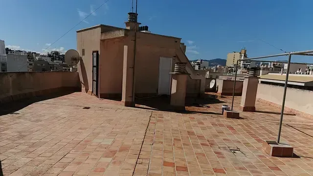 Una azotea con suelo de ladrillo y un edificio al fondo.
