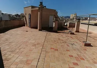 Una azotea con suelo de ladrillo y un edificio al fondo.