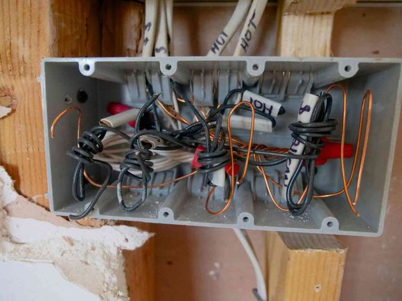 Caja de conexiones eléctricas con cables enredados y conectores de cables en una cavidad de la pared.
