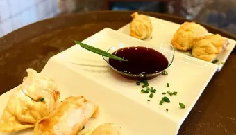 Un plato blanco cubierto con albóndigas fritas y un tazón de salsa para mojar.