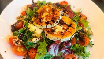 Una ensalada con queso de cabra, tomates, lechuga y nueces en un plato blanco.