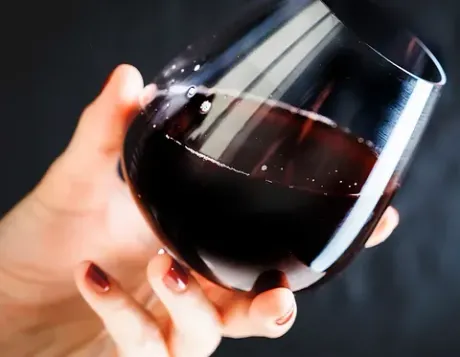 Una mujer sostiene una copa de vino tinto en su mano.
