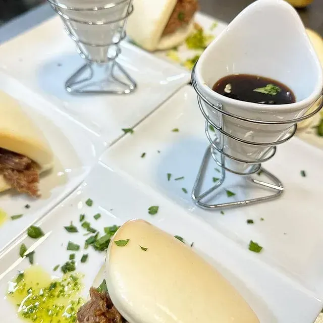 Un plato blanco con un sándwich y una taza de salsa encima.