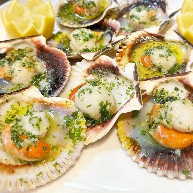 Un plato blanco cubierto con vieiras y rodajas de limón.