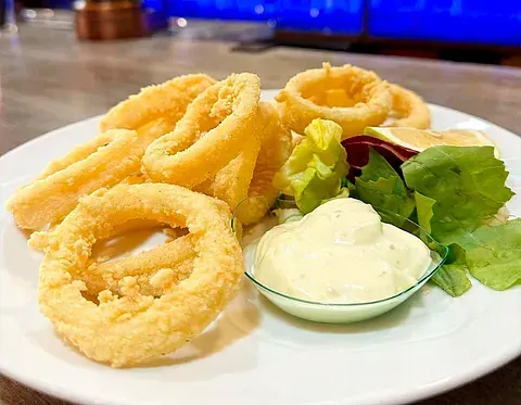 Un plato blanco cubierto con aros de calamares fritos y ensalada.