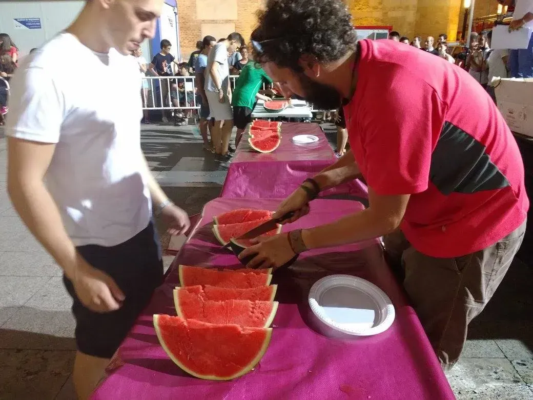 Un hombre con una camisa roja está cortando sandía en una mesa.