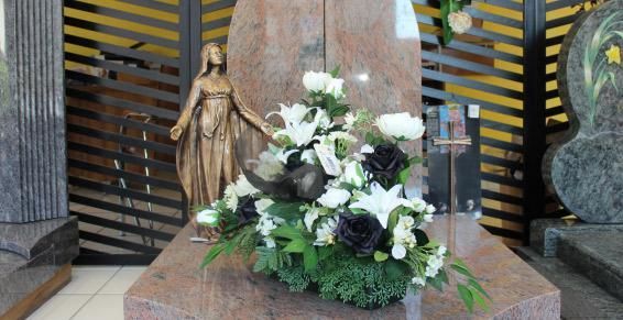 Composition florale sur une pierre tombale en granit rouge, avec une statue en arrière-plan, en intérieur.