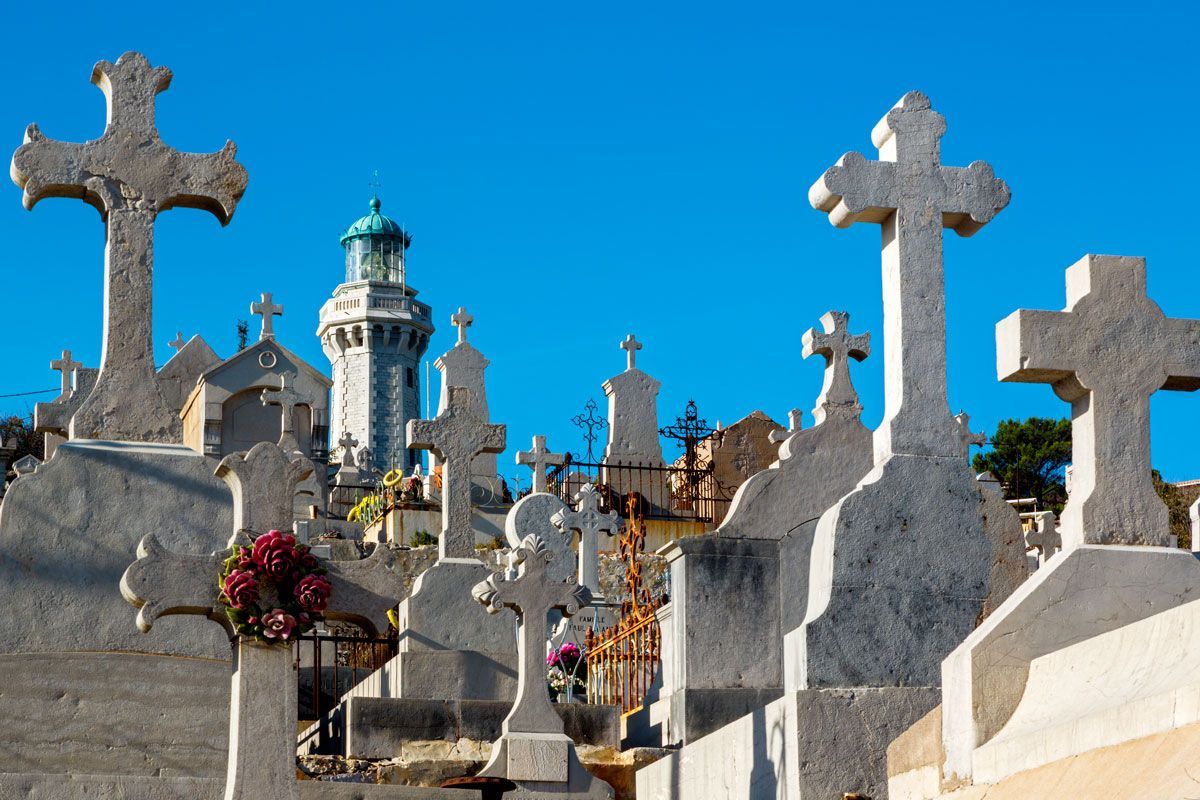 Cimetière avec des croix de pierre blanche et un phare se détachant sur un ciel bleu.