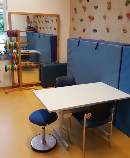 ALT: Therapieraum mit Tisch und Stühlen, Gymnastikmatten und Ringen an einem Ständer