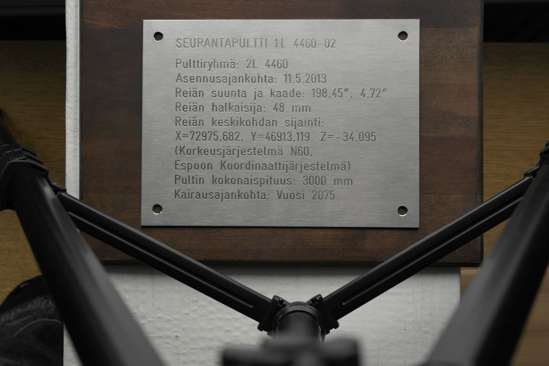 Mikrofonin varret reunustavat seinällä olevaa metallista laattaa, johon on kaiverrettu teksti.