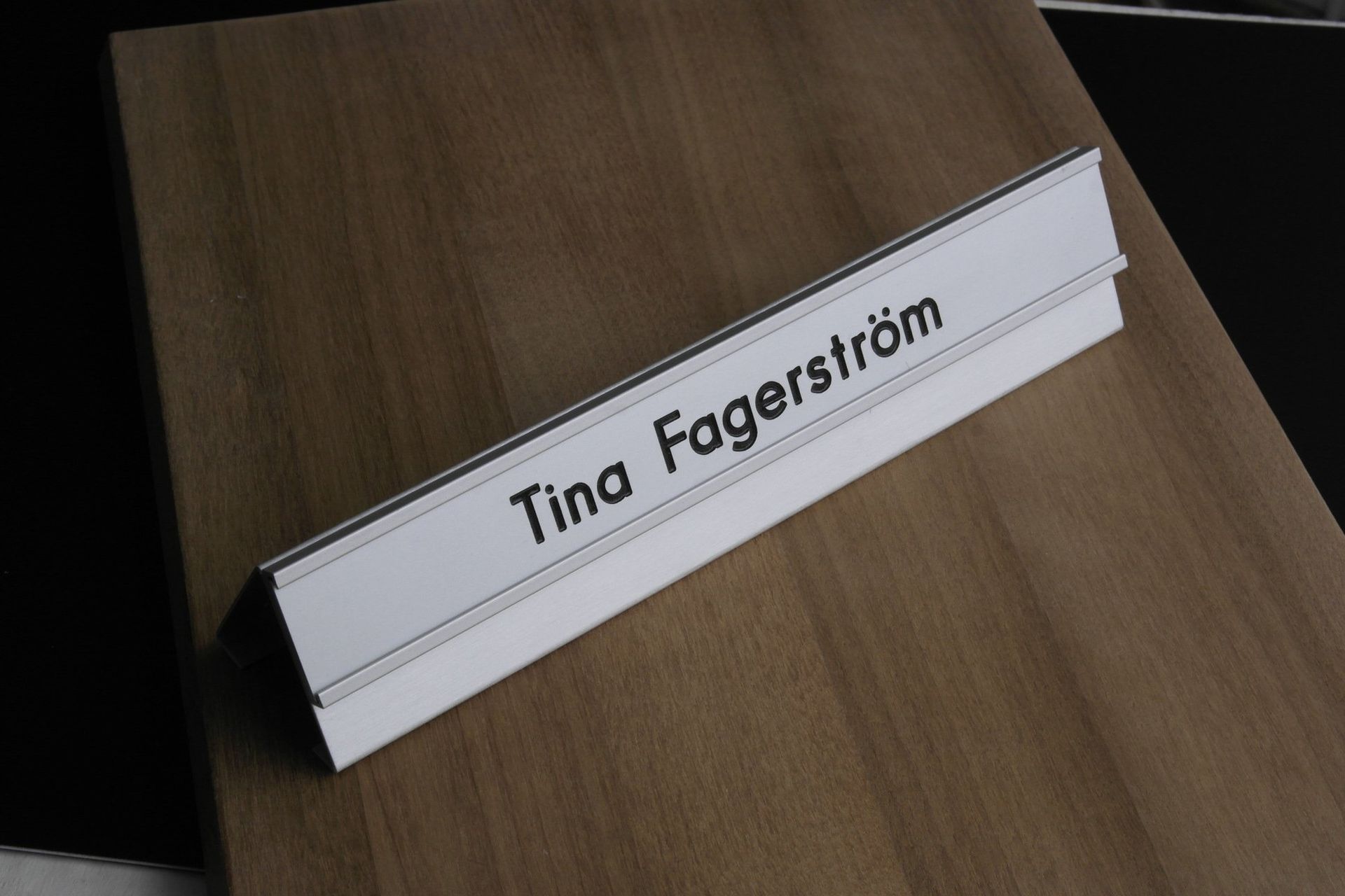 Valkoinen taitettu käyntikortti, jossa lukee ”Tina Fagerström” puupöydällä.