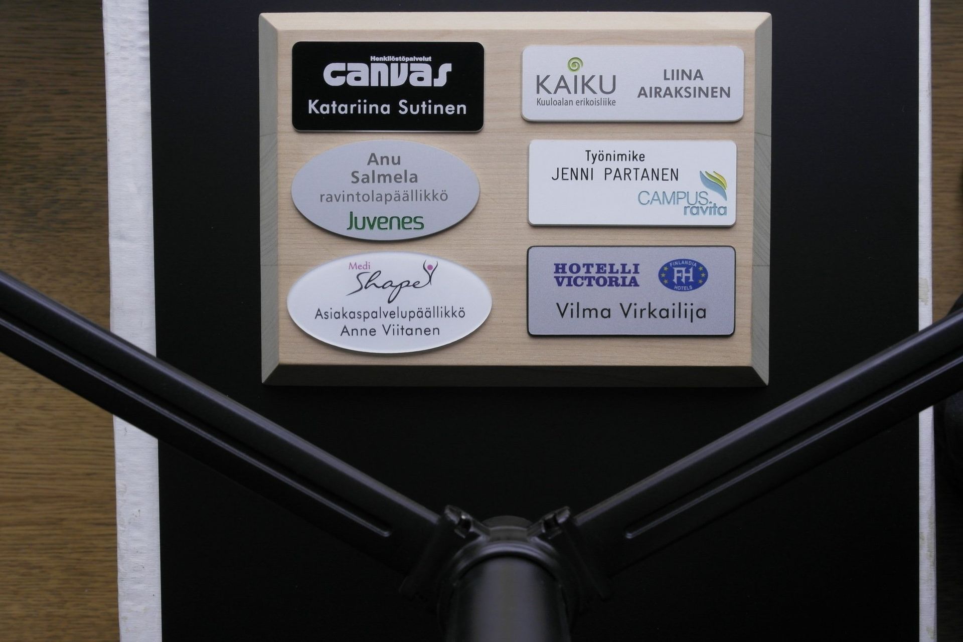 Lähikuva mustasta pyörätuolin rungosta ja seinään kiinnitetystä nimikyltistä, jossa on kuusi etikettiä.