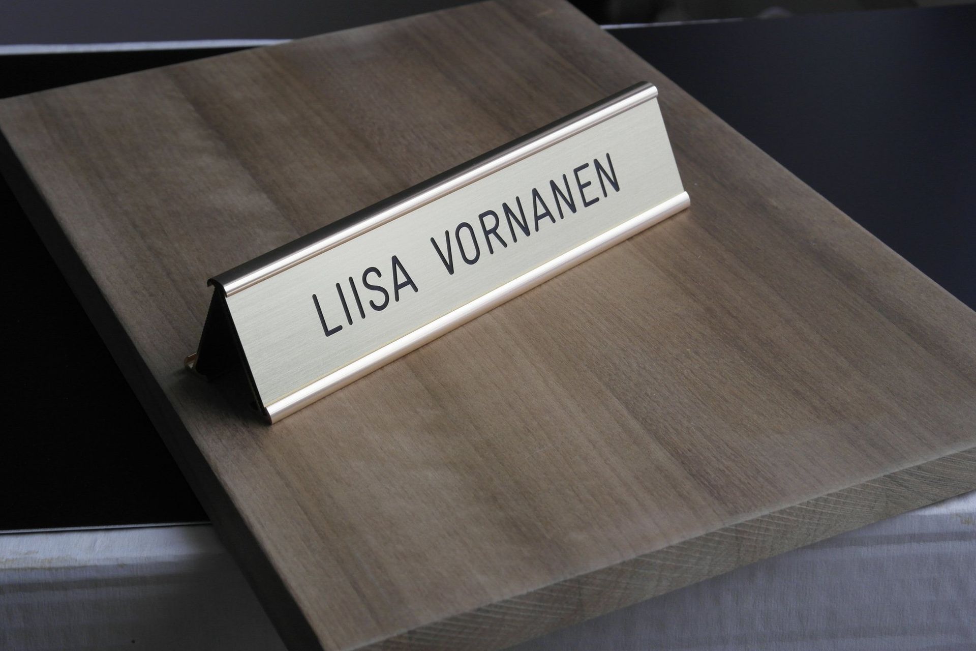 Silver nameplate reading “LIISA VORNANEN” on a wooden desk stand.