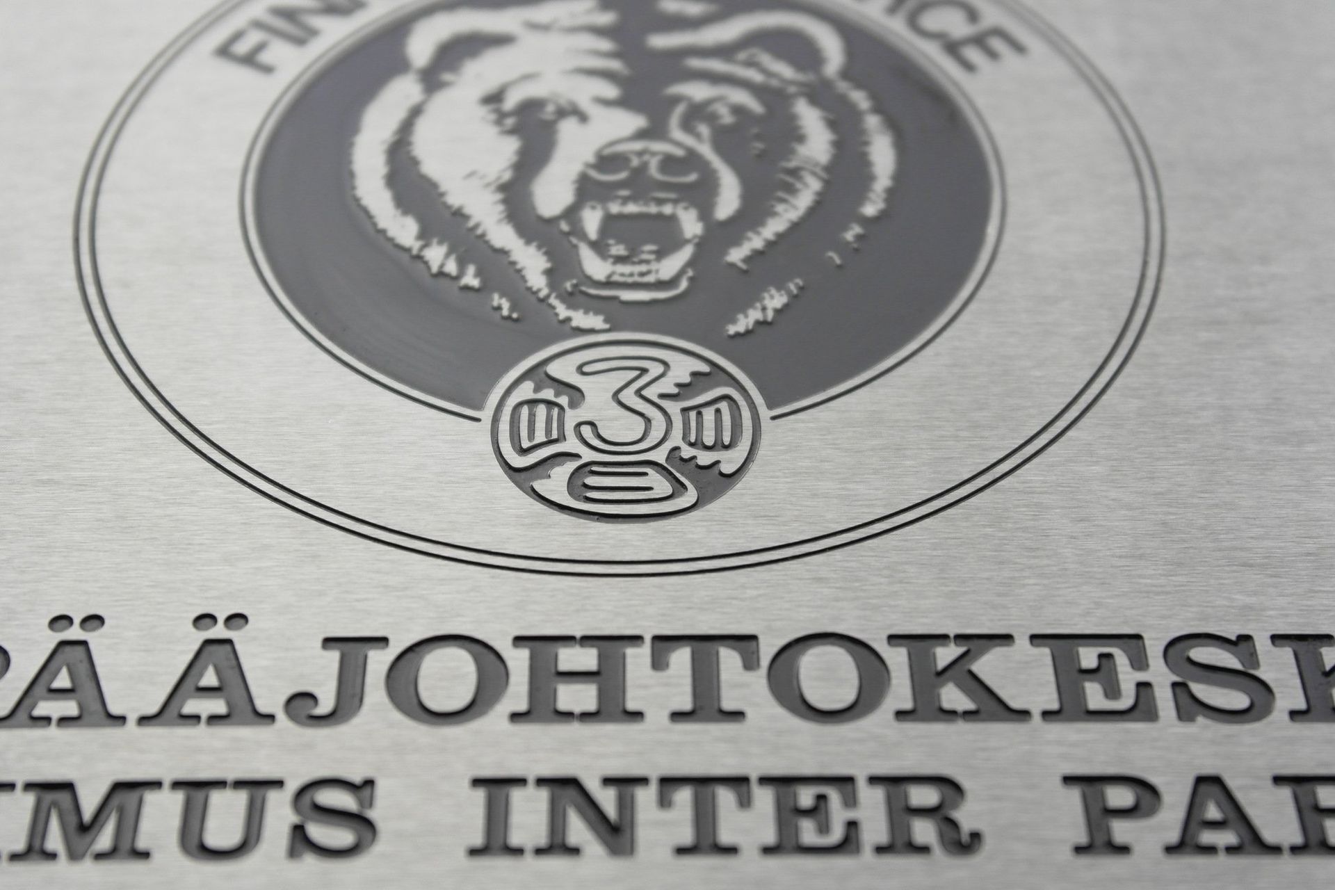 Tunnus, jossa on karjuva karhu ja osittainen teksti harmaalla kyltillä tai asiakirjalla