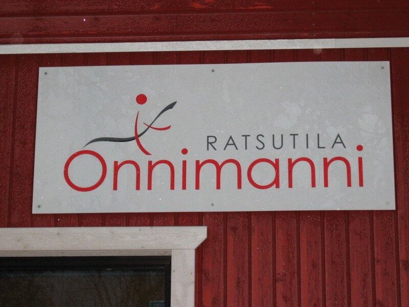 Ratsutla Onnimanni -kyltti valkoisella paneelilla punaista puuseinää vasten