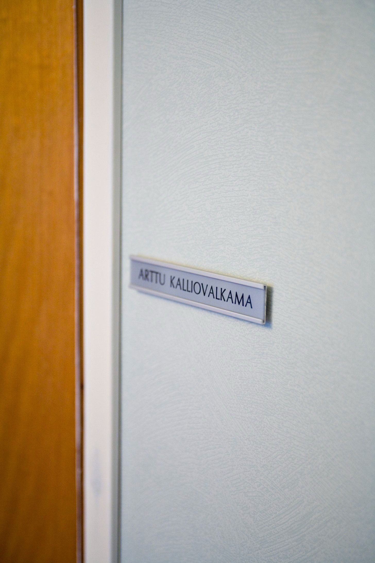 Lähikuva puuoven vieressä olevasta seinälaatasta, jossa lukee harmaalla seinällä 