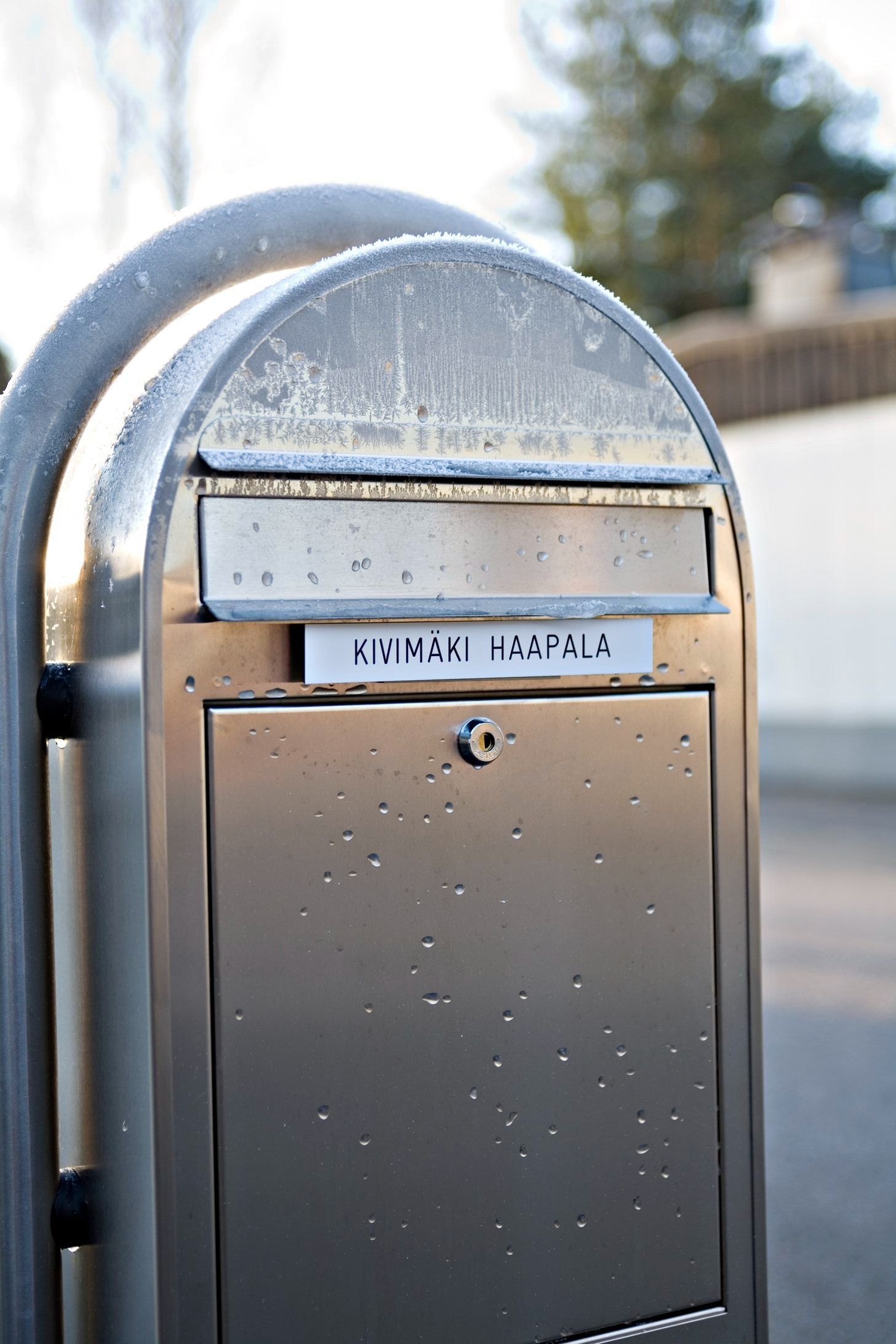 Krominen postilaatikko, jossa on huurretta päällä ja pieni nimilappu, ulkona.